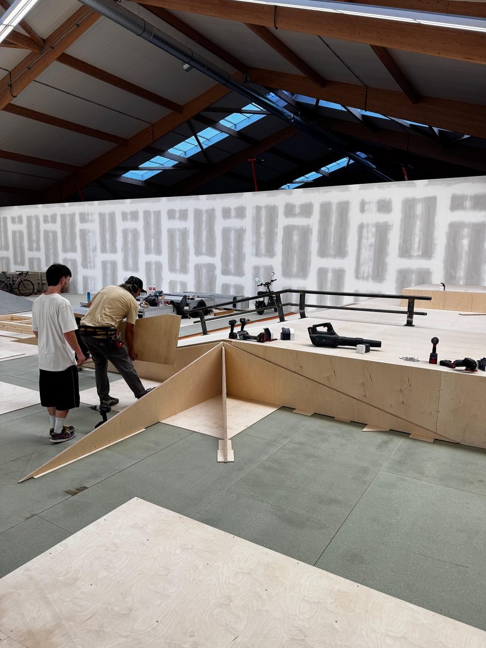 Zwei Leute bauen in der leeren Halle eine Rampe aus Birkenholz auf