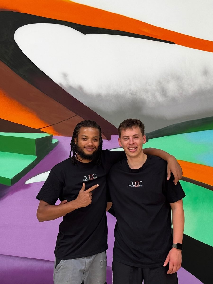 Zwei Betreuer der JOPA Skatehalle in JOPA-Shirts vor der bemalten Wand