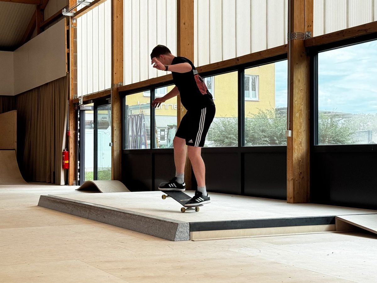 Skater springt über eine niedrige Granitkante vor der Fensterfront