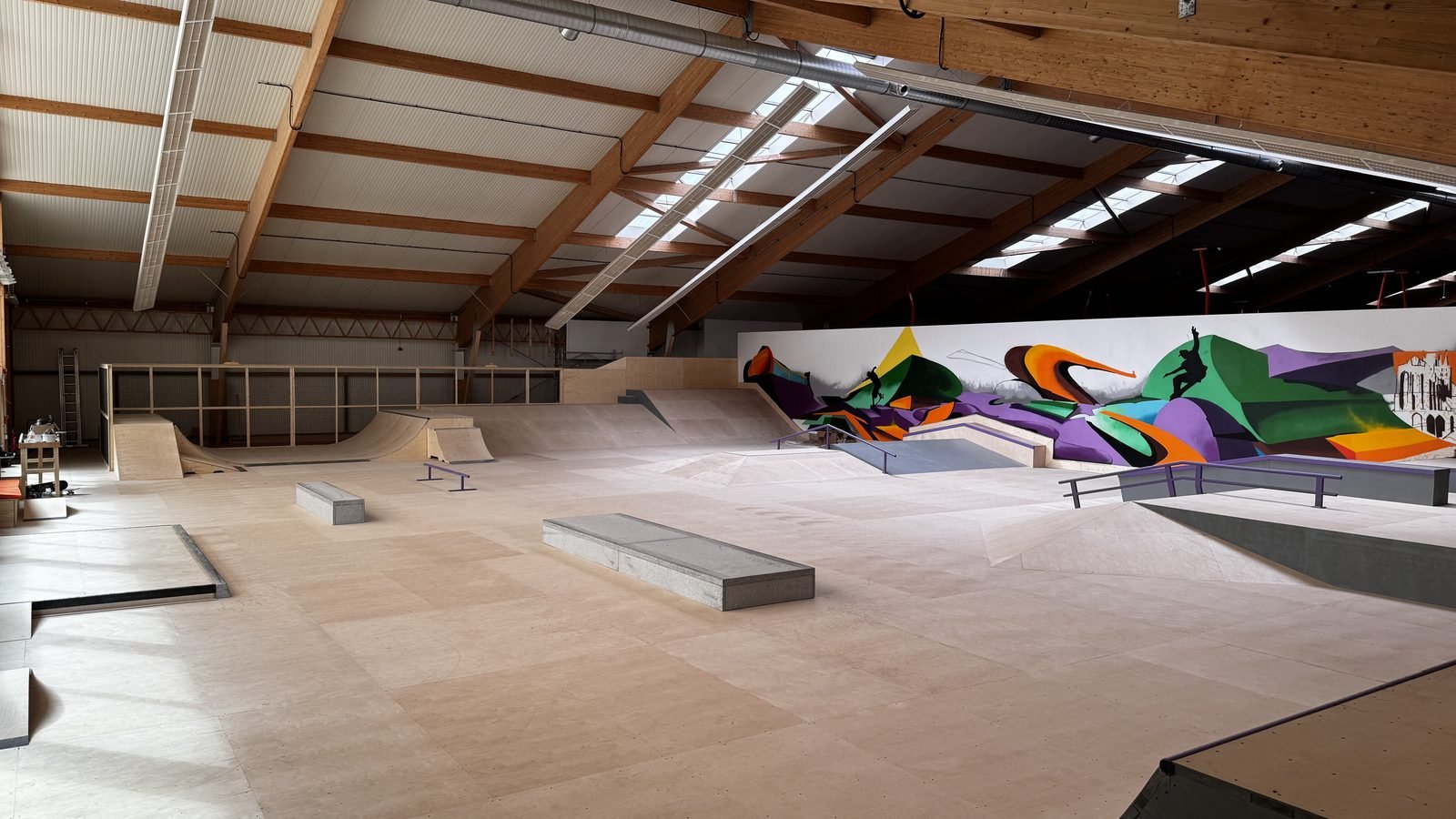 Blick über die gesamte Halle mit Quarter Pipes, Bank und der bemalten Wand